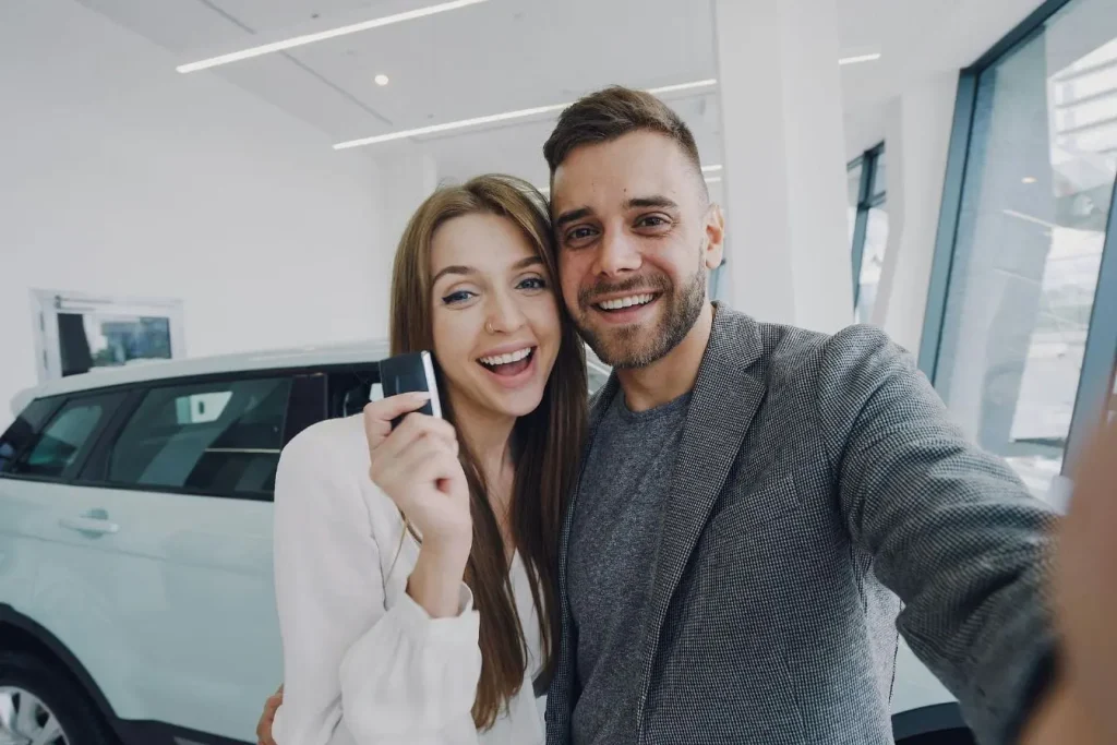 Deux personnes près d’un SUV clair en concession, image qui illustre la remise de clé et la question du délai de réception de la carte grise après achat.