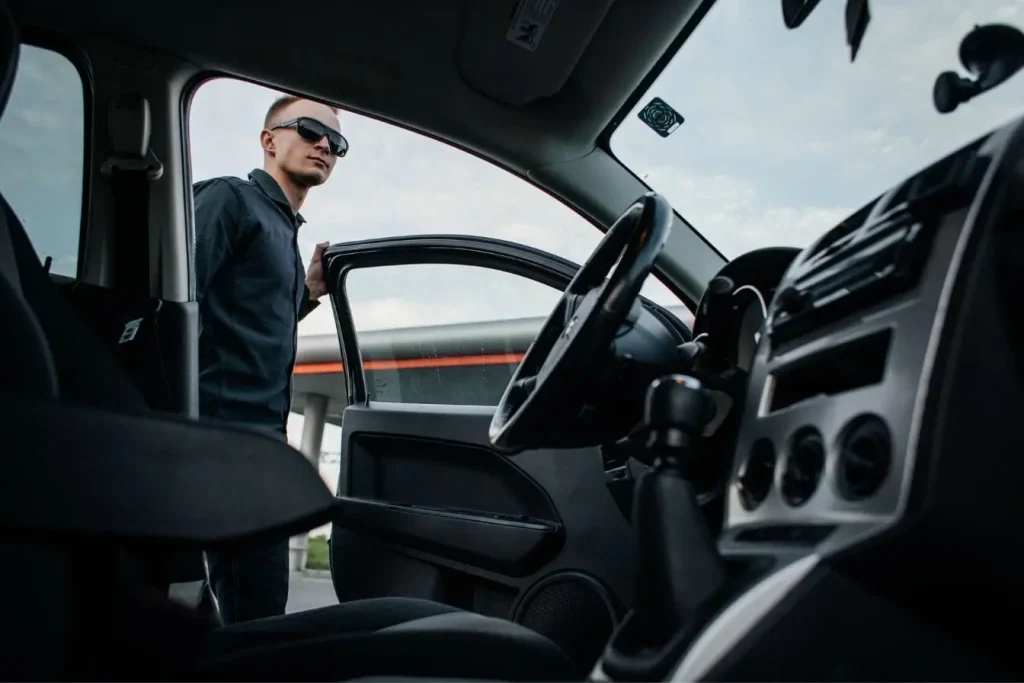 Vue depuis l’intérieur d’une voiture avec portière ouverte et personne en lunettes sombres, image qui illustre les démarches après un vol auprès de la police et de l’assurance.