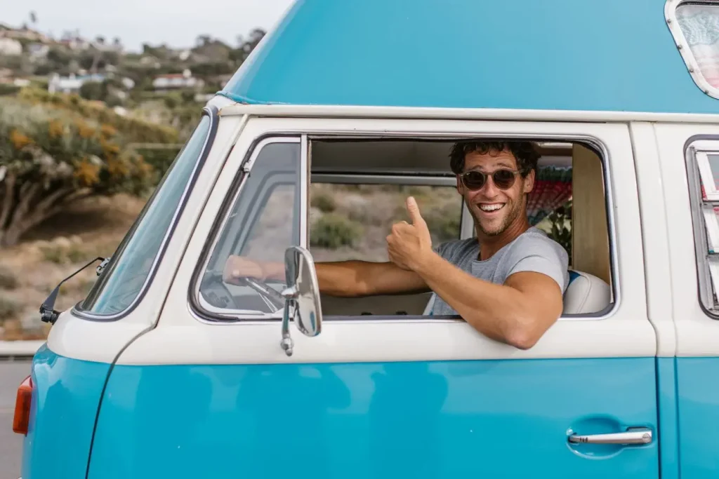 Conducteur souriant dans van vintage bleu et blanc, image qui illustre l’avantage en nature d’un véhicule de fonction utilisé au quotidien.