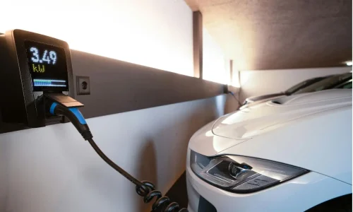 Voiture électrique branchée à une borne murale dans garage moderne, image qui illustre l’installation d’une IRVE à domicile et les aides financières possibles.