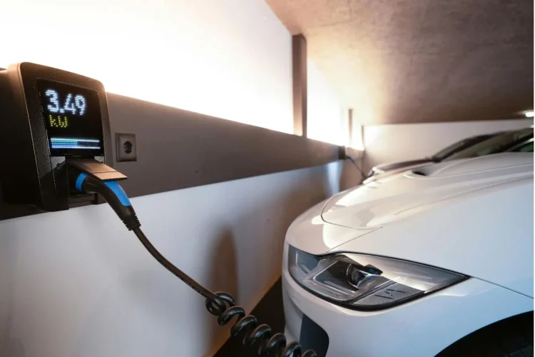 Voiture électrique branchée à une borne murale dans garage moderne, image qui illustre l’installation d’une IRVE à domicile et les aides financières possibles.