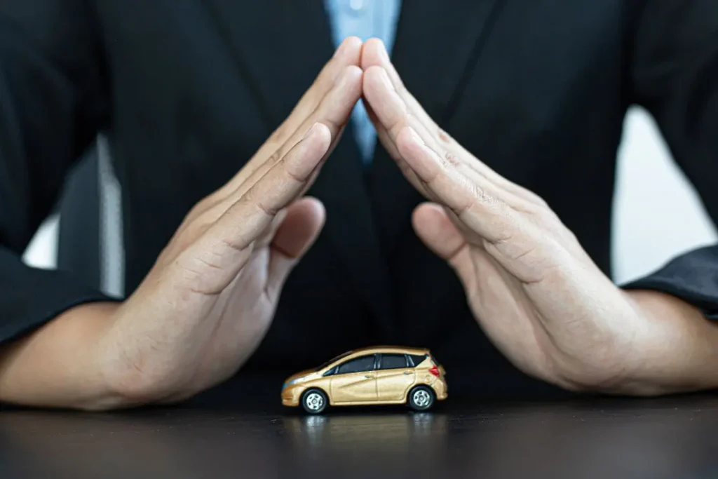 Mains en costume protégeant une petite voiture dorée, image qui illustre le débat sur le malus au poids 2026 et la protection des automobilistes.