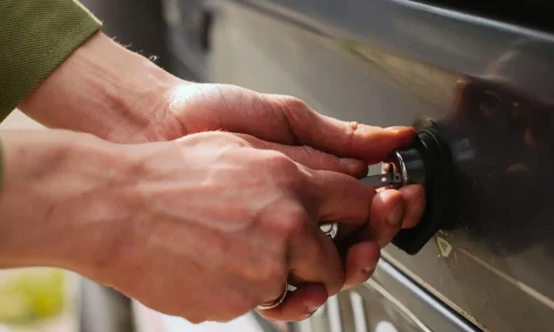 Gros plan sur des mains insérant une clé dans une serrure de voiture, image qui illustre les démarches après un vol auprès de la police et de l’assurance.