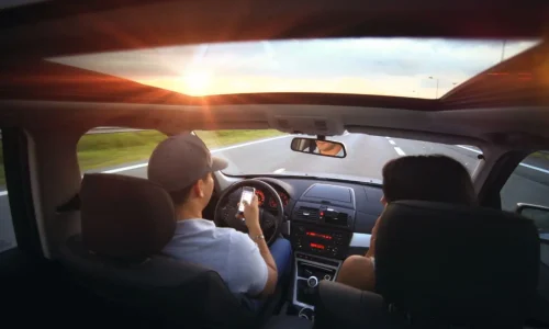 Vue intérieure d’une voiture au coucher du soleil avec conducteur tenant un téléphone, image qui illustre les obligations légales en covoiturage longue distance.