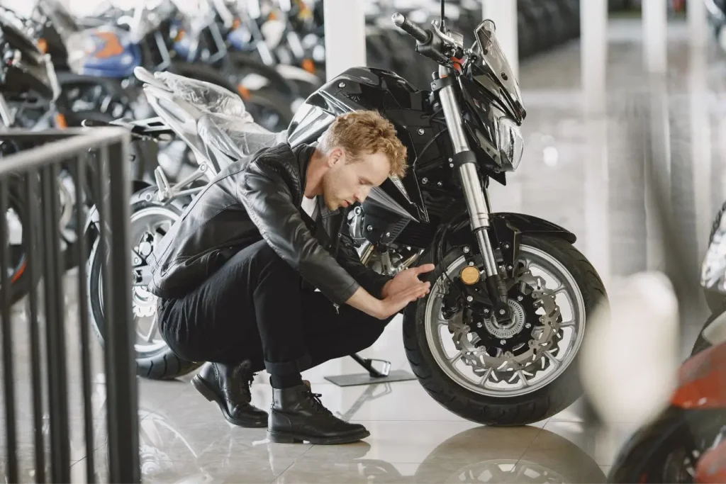 Personne en blouson noir inspectant roue avant de moto, image qui illustre la sécurité offerte par l’ABS moto.