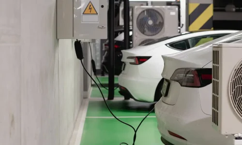 Deux voitures électriques blanches garées sur sol vert, l’une branchée à une borne, image qui illustre l’autonomie réelle influencée par divers facteurs.