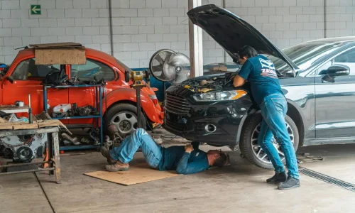 Mécaniciens travaillant sous capot et dessous d’une voiture noire, reflet du coût d’une révision complète en garage.