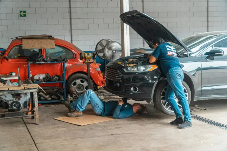 Mécaniciens travaillant sous capot et dessous d’une voiture noire, reflet du coût d’une révision complète en garage.