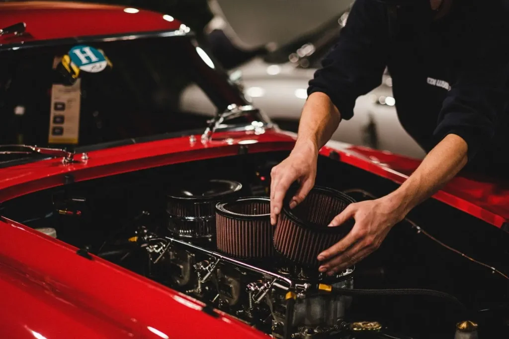 Gros plan sur moteur de voiture classique rouge avec mains ajustant filtre, reflet du coût d’une révision complète en garage.
