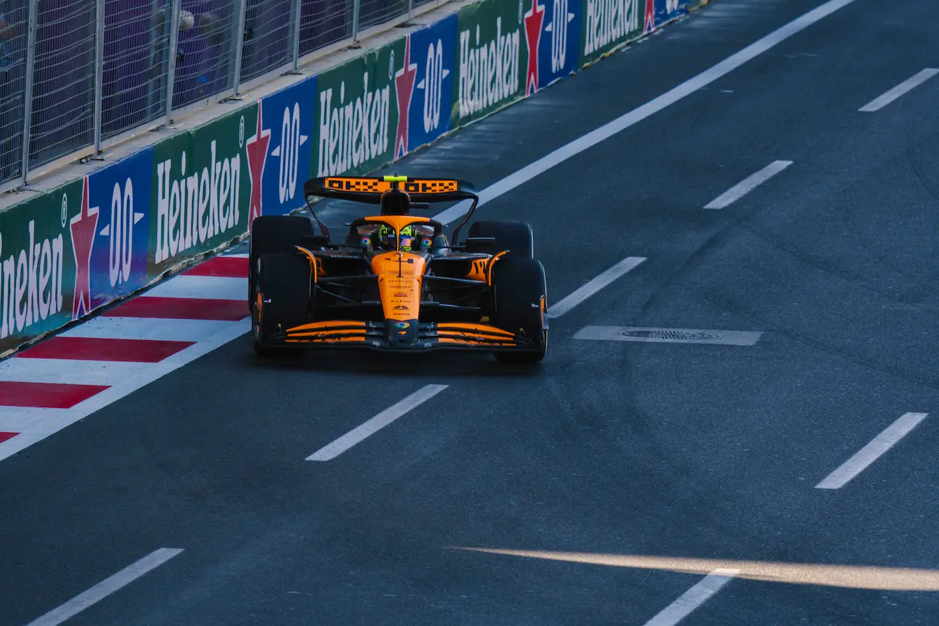 Voiture de course orange et noire lancée sur circuit, reflet de l’écurie de F1 la plus titrée de l’histoire.