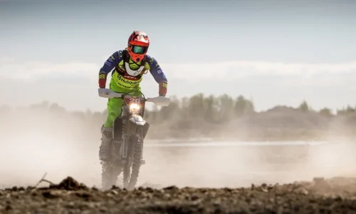 Pilote en combinaison verte et bleue sur moto tout-terrain, reflet de l’intensité de la vitesse moto comparée à l’endurance.