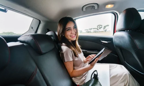 Personne assise à l’arrière d’une voiture utilisant une tablette, symbole des trajets longue distance facilités par le covoiturage.