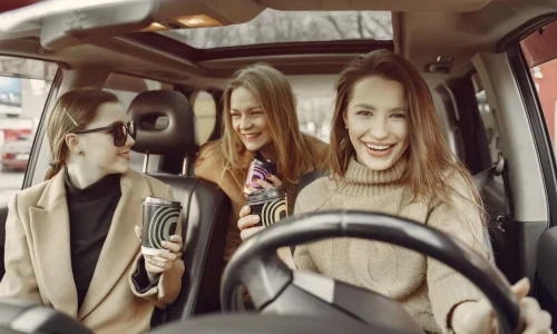 Trois personnes assises dans une voiture avec cafés à la main, symbole des usages conviviaux liés à l’autopartage urbain.