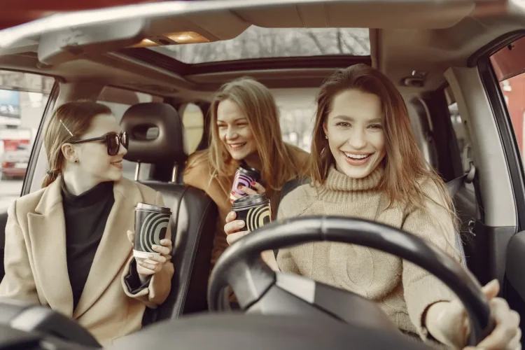 Trois personnes assises dans une voiture avec cafés à la main, symbole des usages conviviaux liés à l’autopartage urbain.