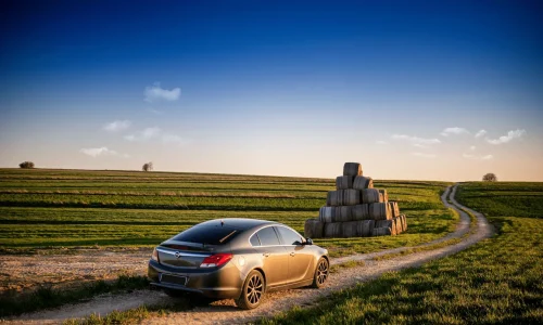 Voiture sombre garée près de bottes de foin, symbole des assurances au kilomètre adaptées aux petits rouleurs.