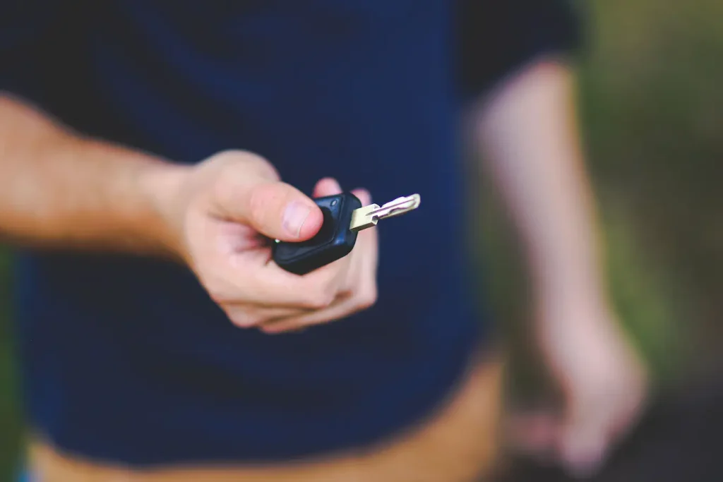Main tenant clé de voiture noire avec boîtier, symbole des pratiques de mobilité partagée entre autopartage et location entre particuliers.