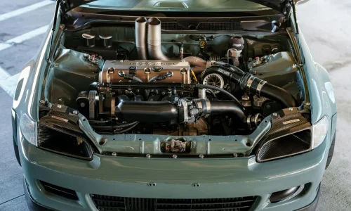 Un capot ouvert sur un compartiment moteur propre et détaillé d'une voiture grise, montrant les pièces mécaniques et le turbocompresseur.
