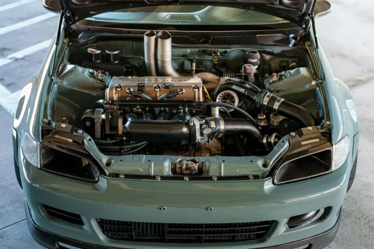 Un capot ouvert sur un compartiment moteur propre et détaillé d'une voiture grise, montrant les pièces mécaniques et le turbocompresseur.