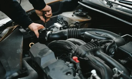 Mécanicien intervenant sous le capot d’une voiture avec un tournevis, illustrant la recherche des causes de vibrations et de secousses moteur au ralenti