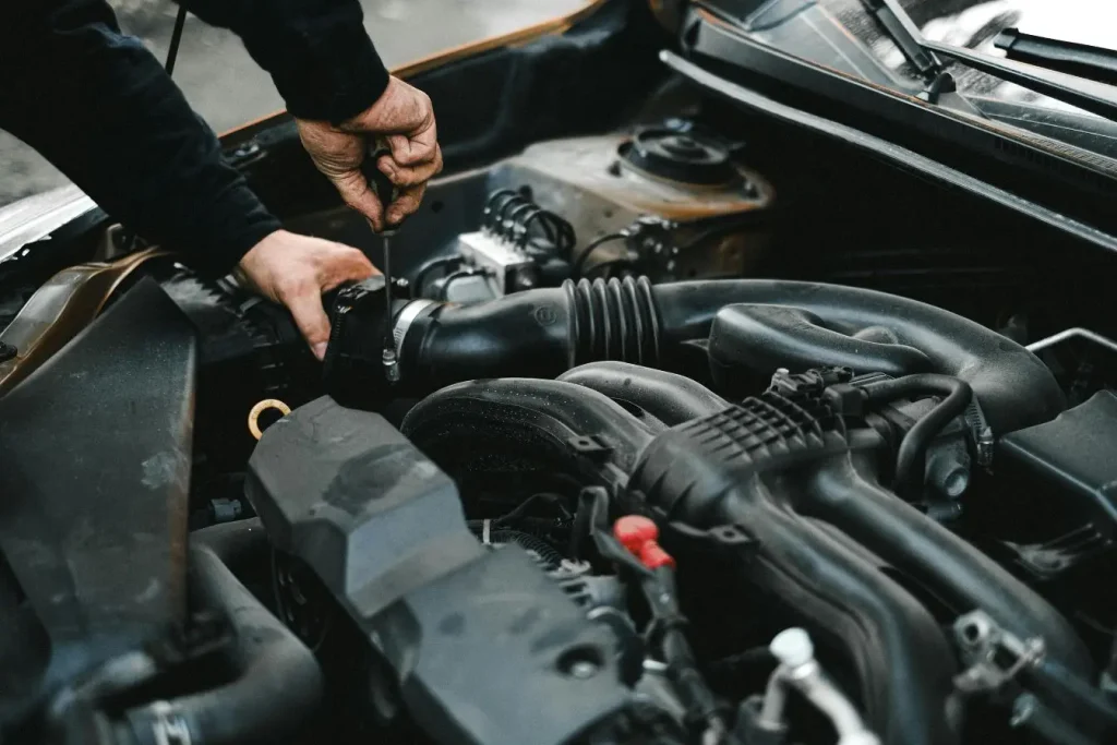 Mécanicien inspectant le compartiment moteur d’une voiture avec un outil, illustrant la recherche d’une fuite pouvant provoquer une odeur d’essence persistante
