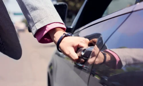 Main en costume ouvrant portière de voiture sombre, symbole des pratiques liées à l’autopartage et à la location entre particuliers.