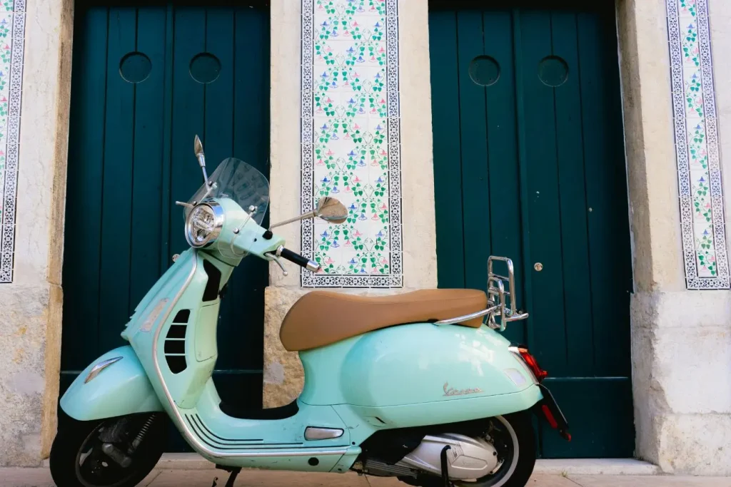 Vespa turquoise garée devant portes décorées, symbole de mobilité urbaine et de l’autonomie moyenne d’un scooter électrique.