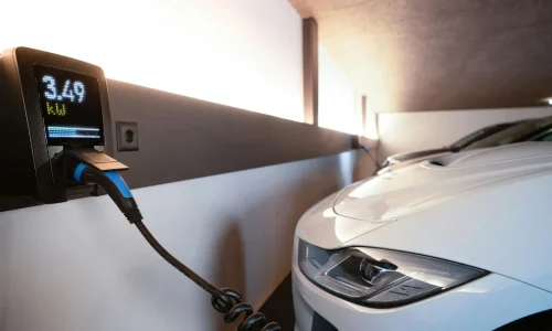 Voiture électrique blanche branchée à borne murale, symbole des pratiques liées au temps de charge sur prise domestique.