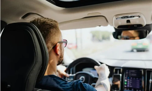 Conducteur concentré tenant volant dans habitacle moderne, symbole des réflexions sur alternatives à la voiture individuelle en ville.