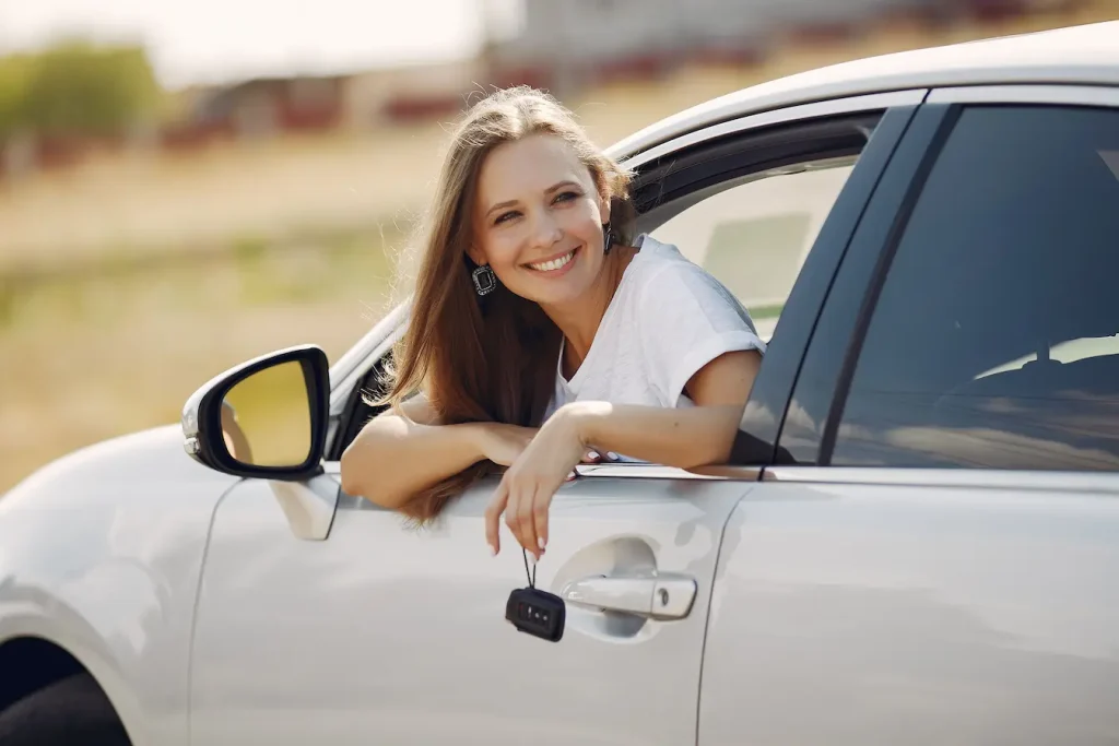 Personne en chemise blanche tenant clé de voiture par la fenêtre, symbole des assurances au kilomètre pour petits rouleurs.