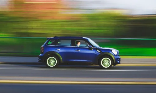 Une voiture bleue roule rapidement sur une route en créant un effet de filé, illustrant un bruit de flottement à l'accélération.