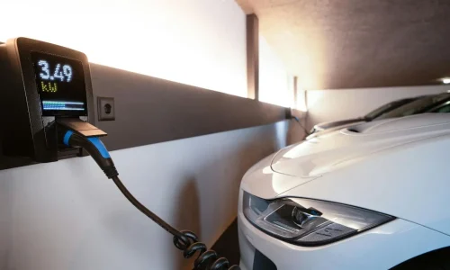 Voiture électrique blanche branchée à borne murale, symbole des interrogations sur la durée de vie moyenne d’une batterie.