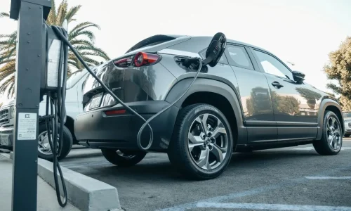 Voiture hybride branchée à une borne de recharge sur un parking, illustrant les problèmes de batterie ou de recharge parmi les pannes les plus fréquentes